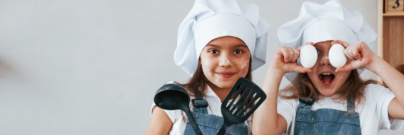 Two kids in chefs outfits in the kitchen cooking